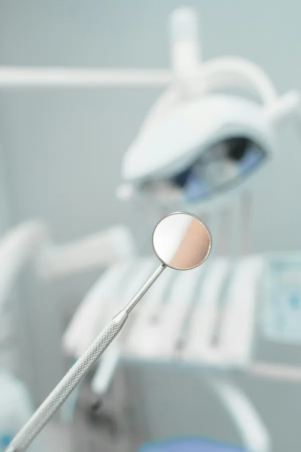 Espelho clínico em primeiro plano e cadeira odontológica ao fundo