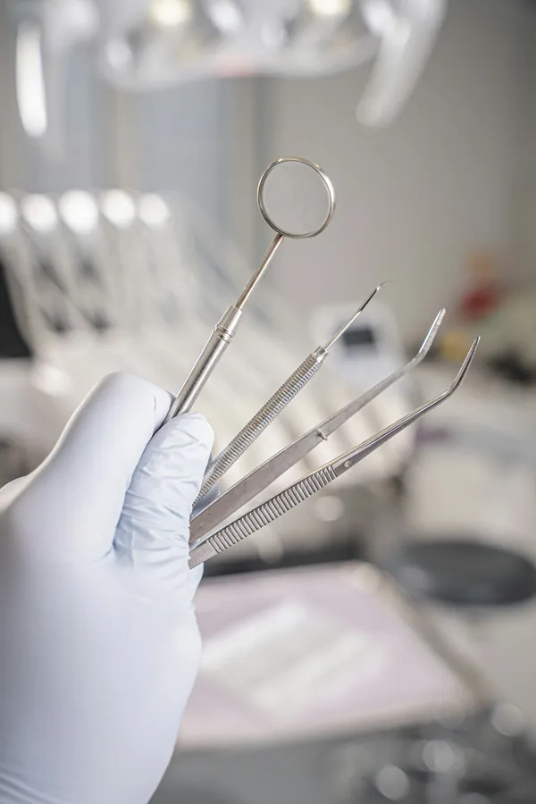 Mão com luva segurando instrumentais odontológicos